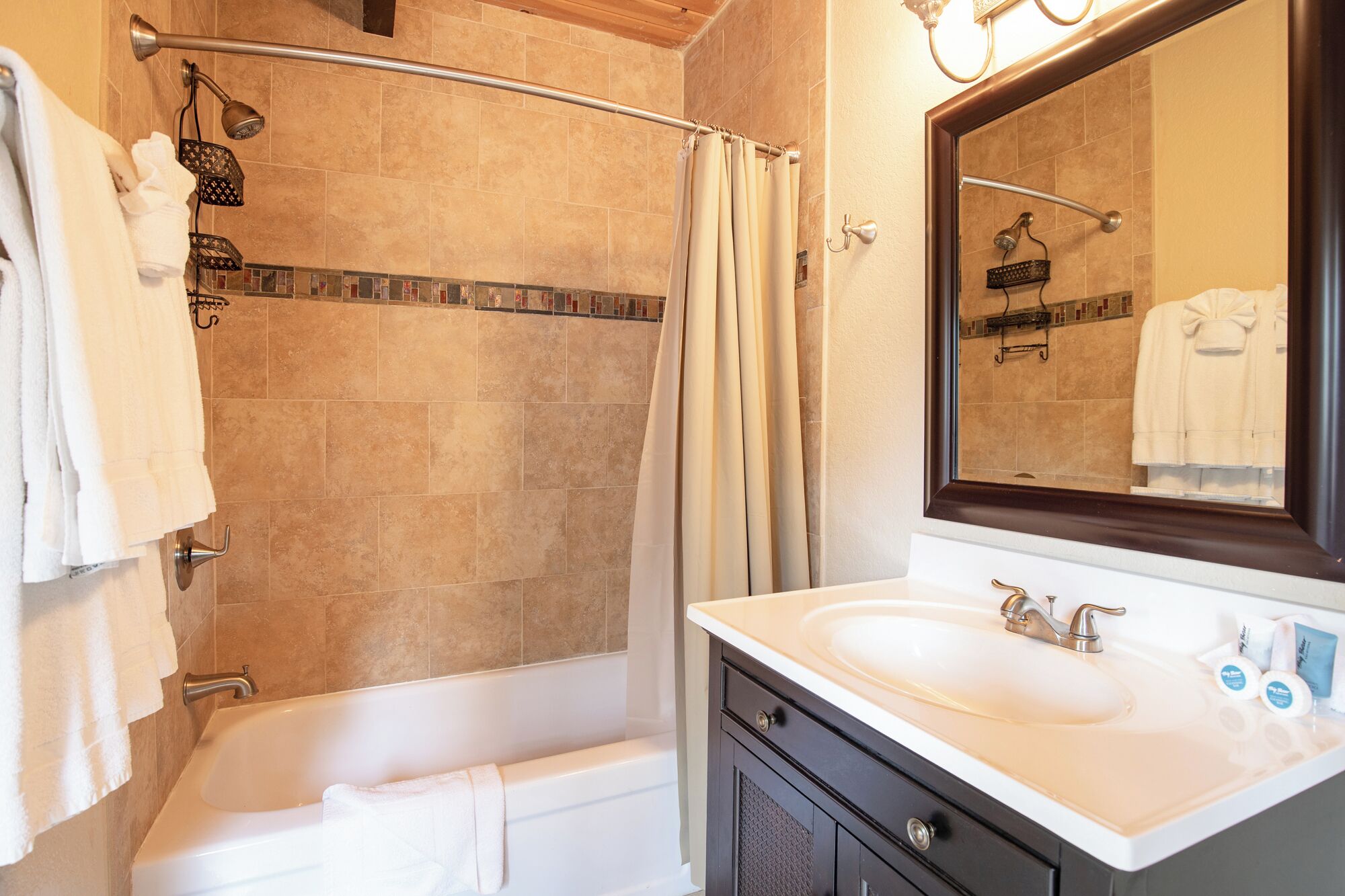 Un baño con bañera, ducha con puerta de cristal, lavabo con espejo y toallas colgadas en la pared.