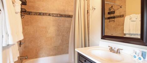Un baño con bañera, ducha con puerta de cristal, lavabo con espejo y toallas colgadas en la pared.