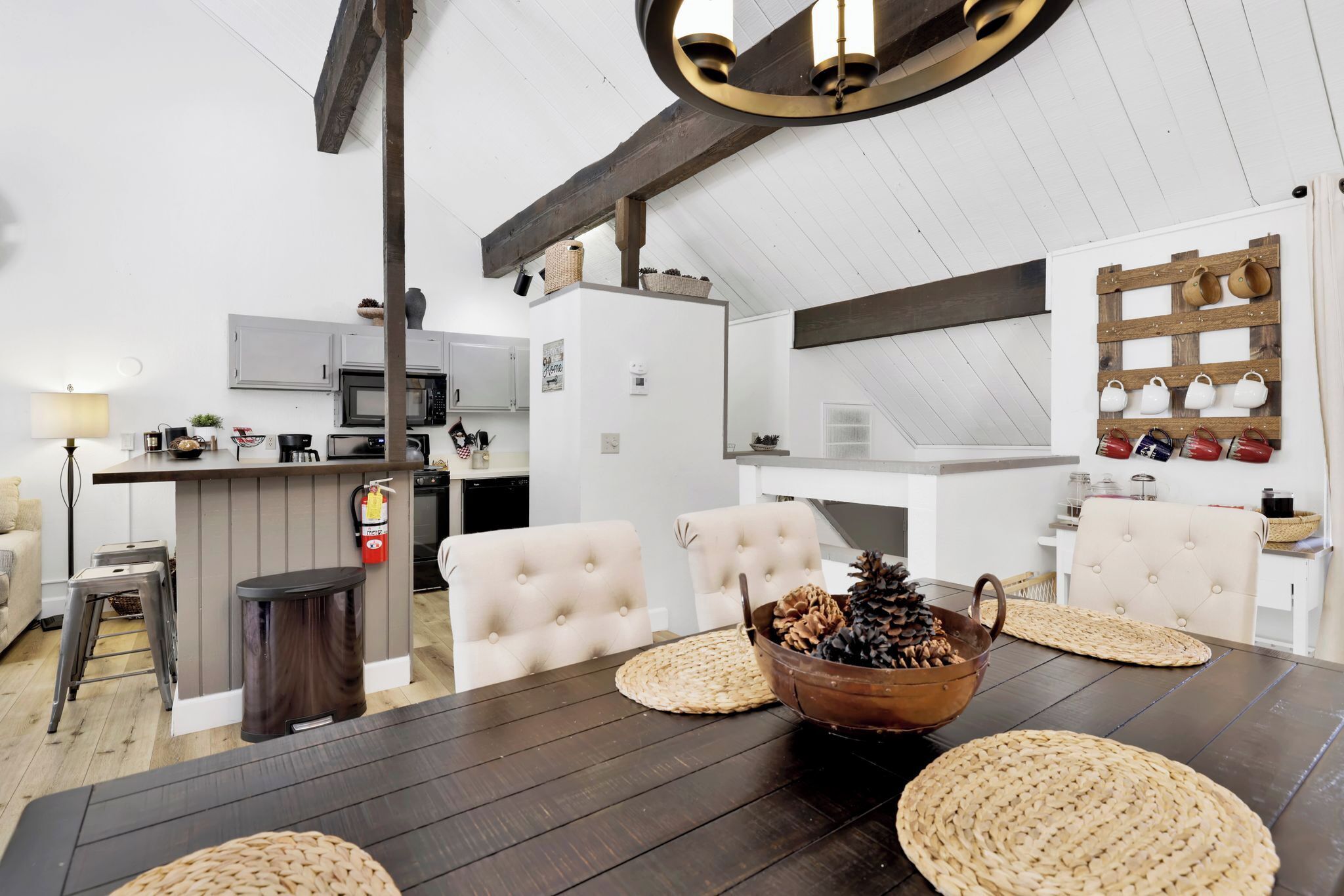 A modern kitchen with white cabinets, a microwave, and a coffee machine. There is a dining table with woven placemats and a decorative bowl.