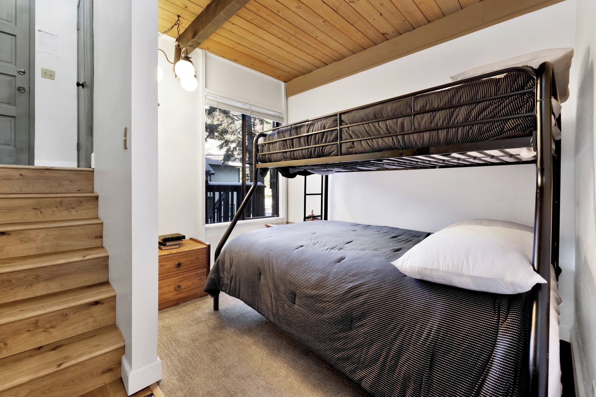 Ein Stockbett mit gestreifter Matratze, einem weißen Kissen und einer Holztreppe.