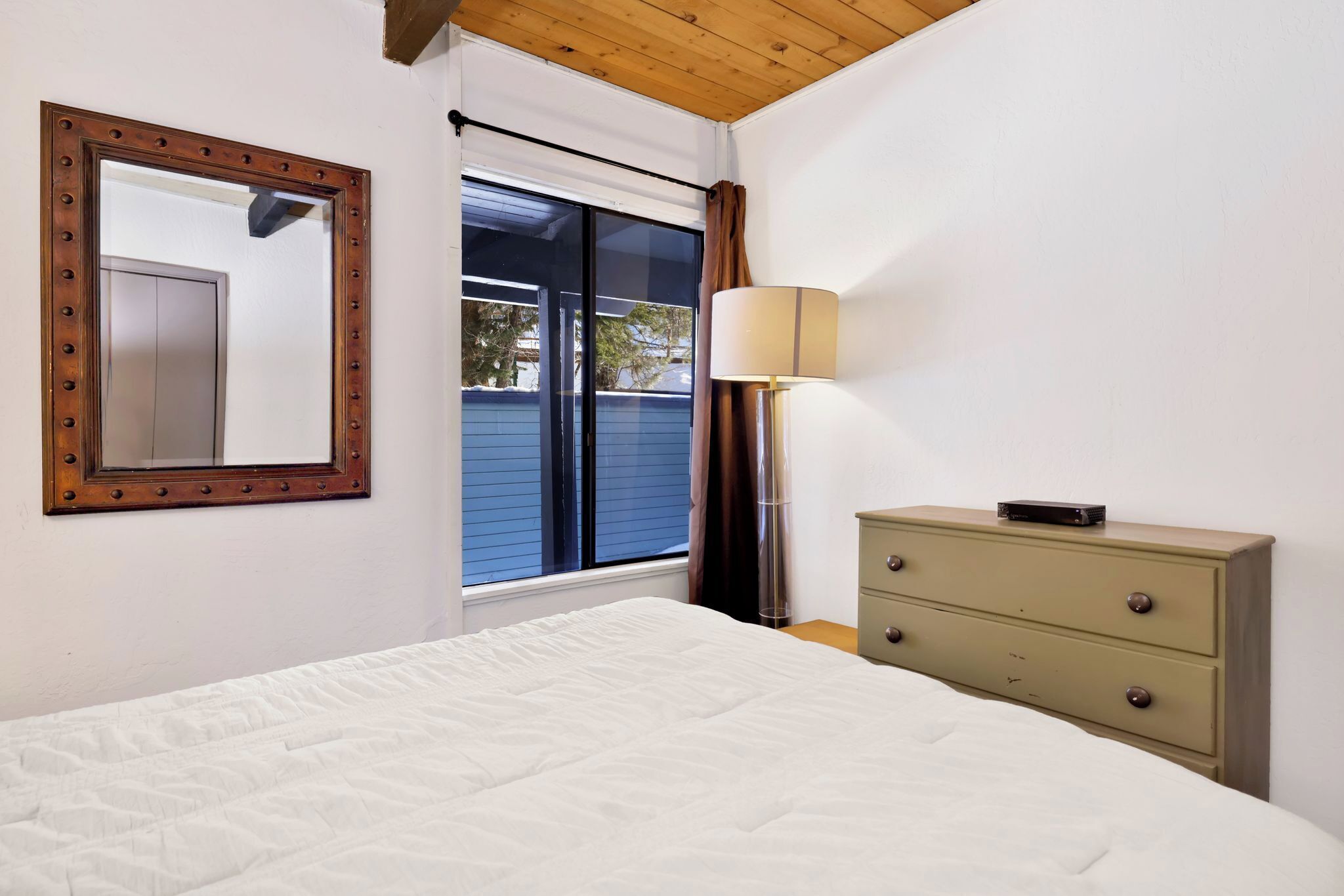 Un dormitorio con una cama grande, un aparador, un espejo, una ventana con cortinas y una lámpara.
