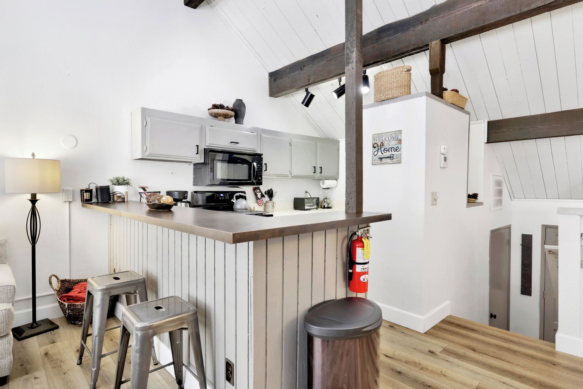 Una cocina moderna con armarios blancos, una isla central con taburetes, microondas y extintor.