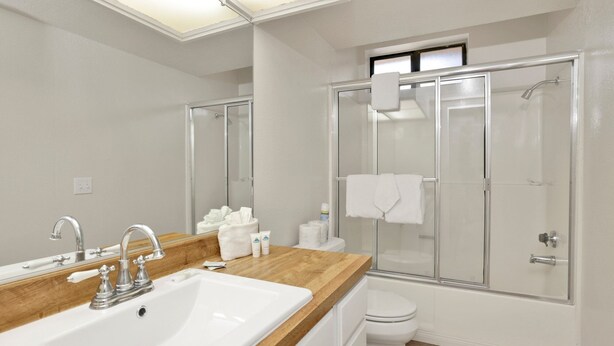 A modern bathroom with a wooden vanity, a sink, a toilet, and a glass-enclosed shower. - Restmoore #2425 (Big Bear Lake)