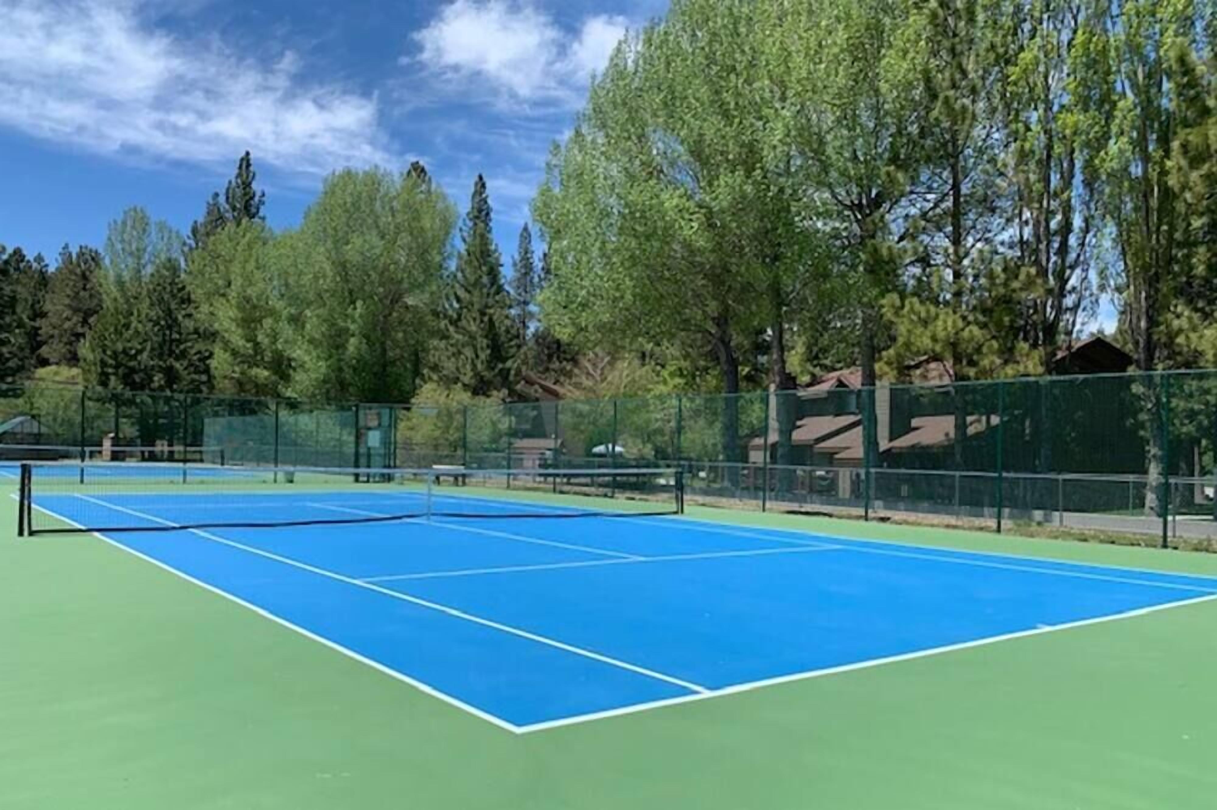 Una cancha de tenis al aire libre rodeada de árboles y una valla.
