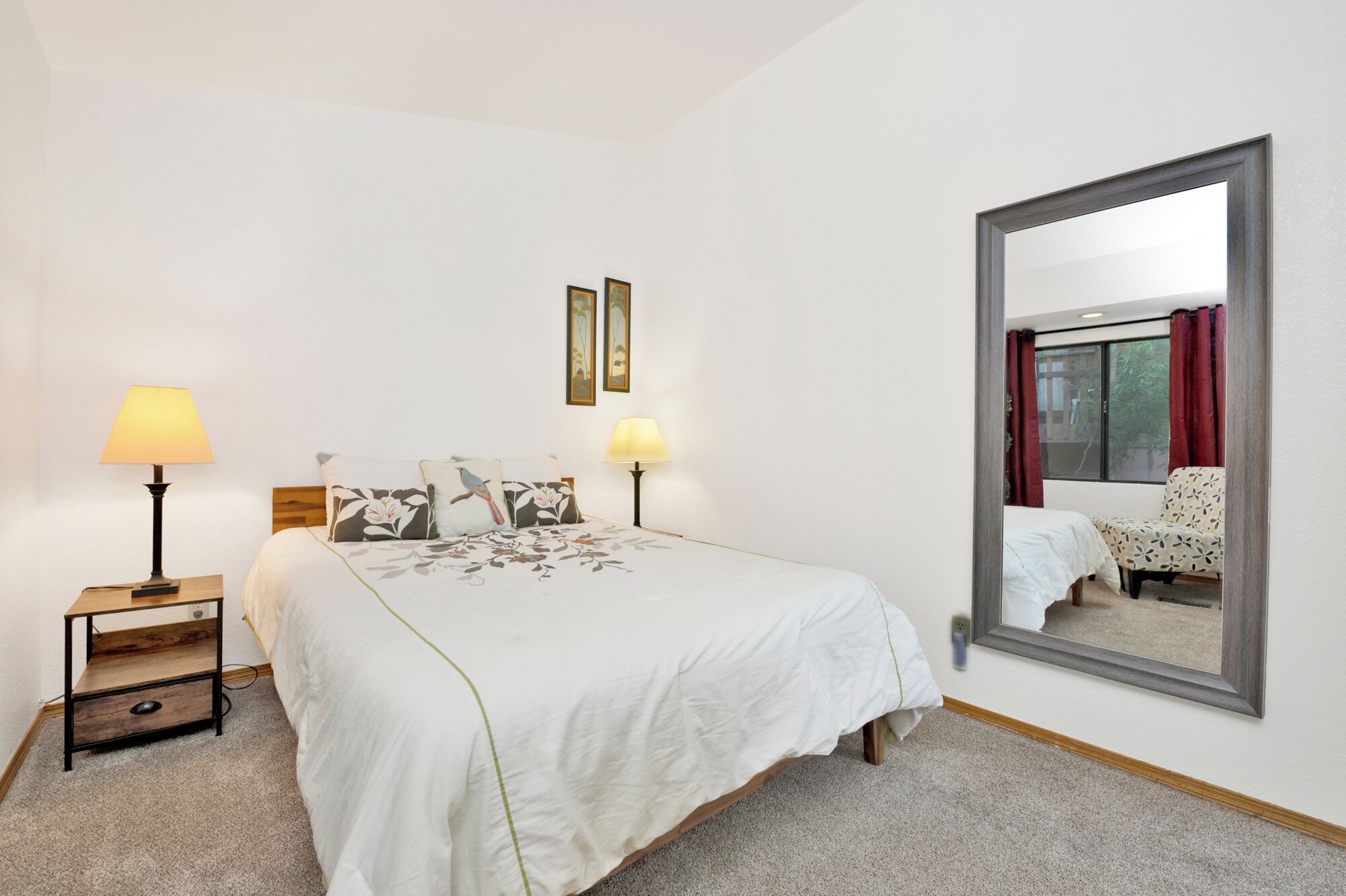 Hotelkamer met een groot bed, twee bedlampen, een klein houten nachtkastje, een spiegel en een raam met gordijnen.
