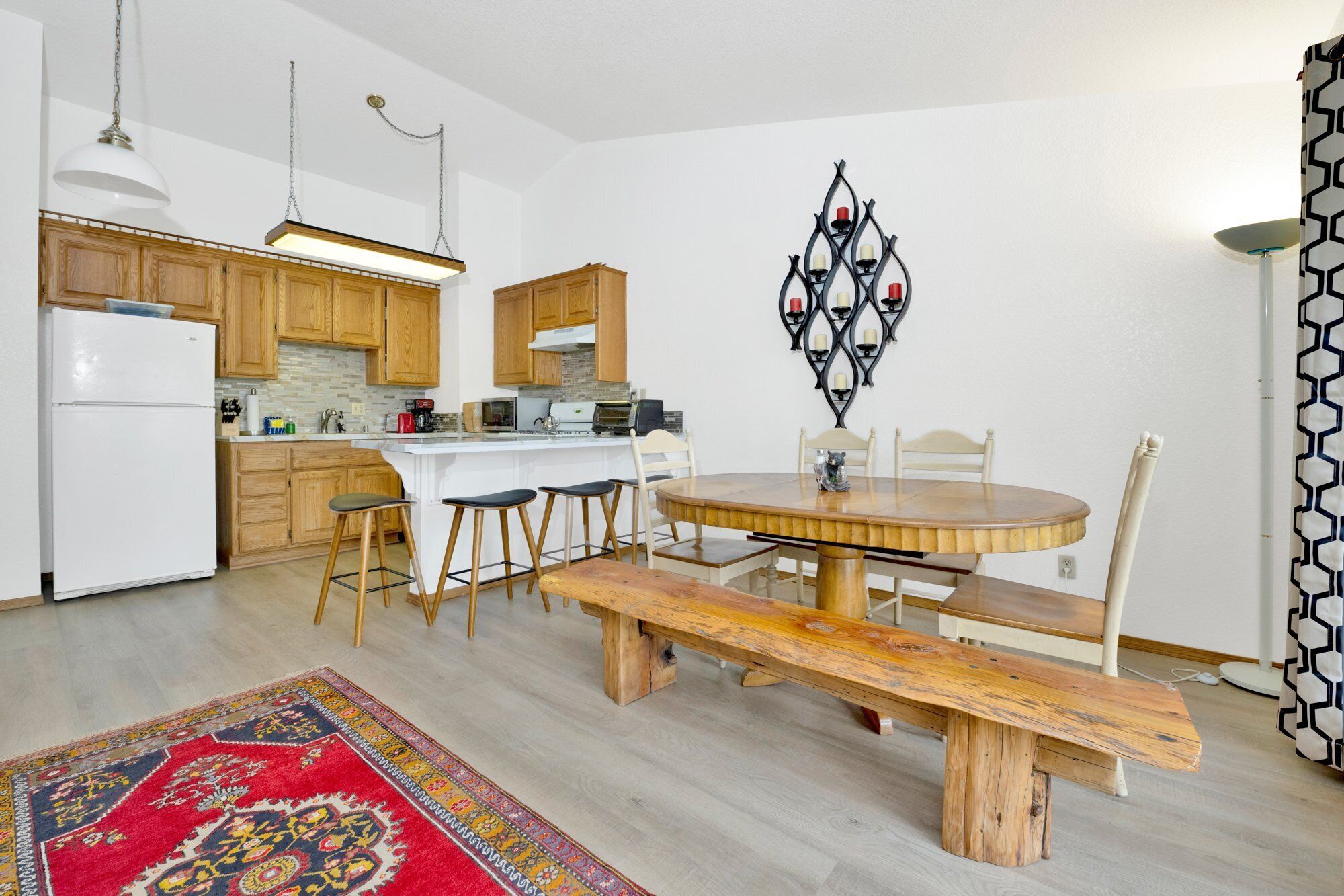 A kitchen with wooden cabinets, a white refrigerator, a dining table with four chairs, and a bench.