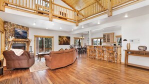 A spacious living area with a fireplace, a stone fireplace surround, a large brown sofa, a dining area with a wooden table and chairs, and a kitchen with a stone island and bar stools. - Cozy Lakeview Hideaway #2261 (Fawnskin)