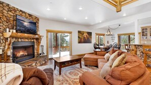 A cozy living room with a stone fireplace, comfortable seating, and large windows offering a view of the outdoors. - Cozy Lakeview Hideaway #2261 (Fawnskin)