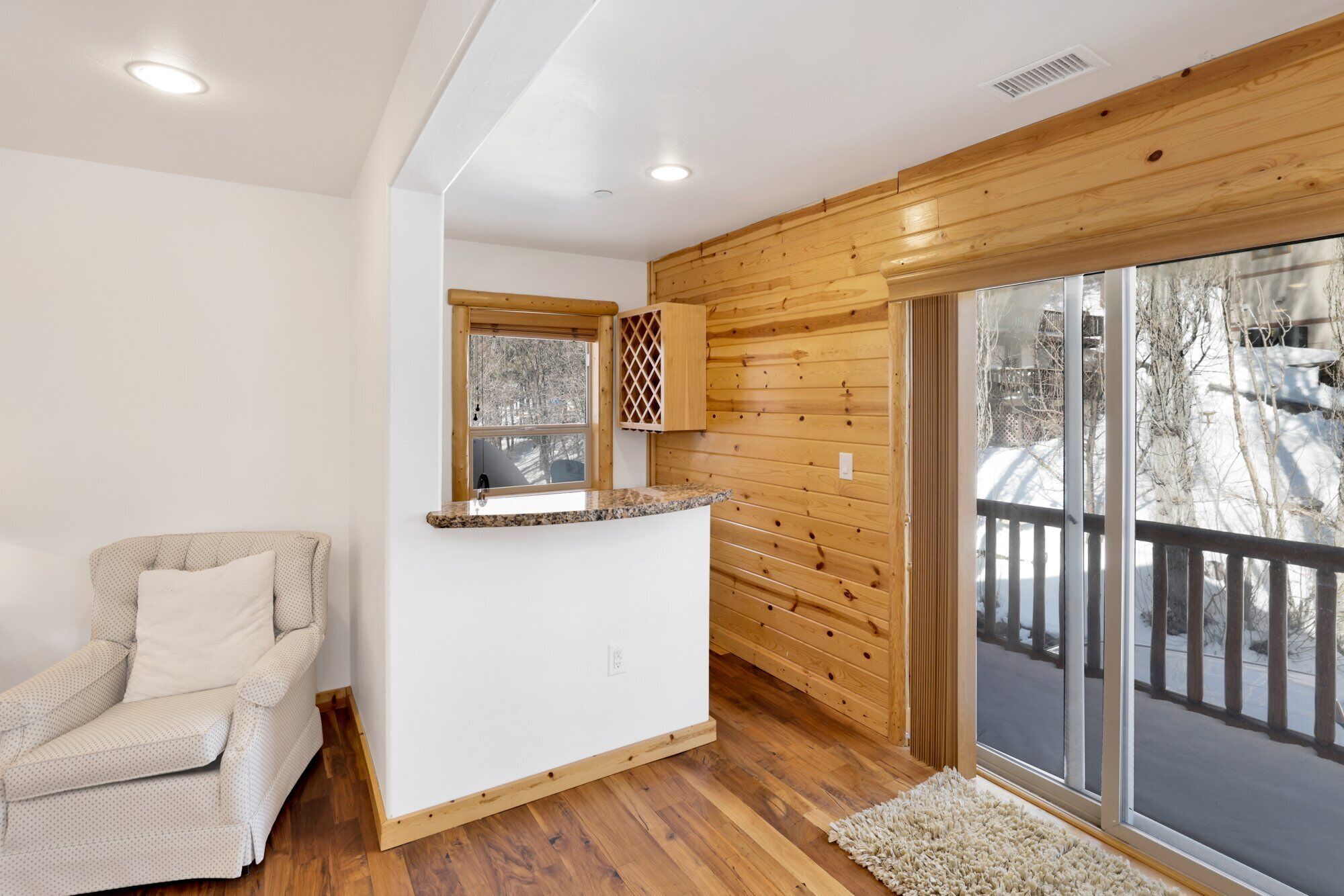 Una habitación acogedora con techo de madera, una encimera de cocina integrada, un sillón mullido y un amplio ventanal corredero que da a un balcón.