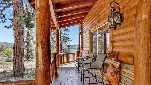 A wooden cabin with a porch, a table, chairs, and a bear statue. - Cozy Lakeview Hideaway #2261 (Fawnskin)