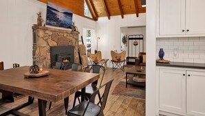 A rustic interior with a stone fireplace, wooden dining table, and white cabinetry. - Twin Pines Lodge #2458 (Big Bear Lake)