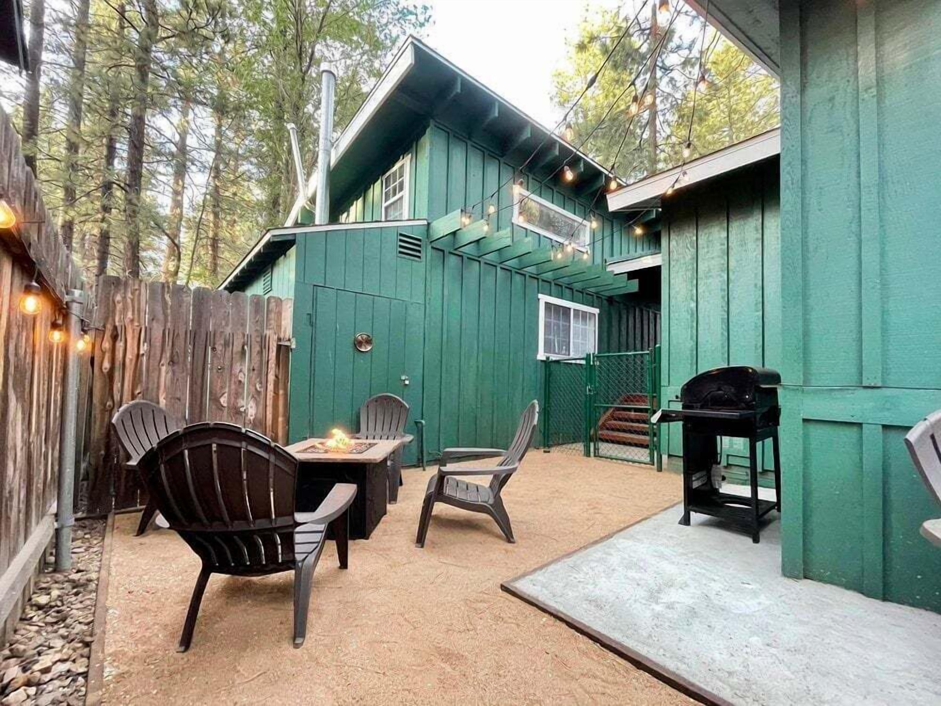 Un bâtiment en bois de couleur verte, doté d’un patio couvert, d’un espace extérieur aménagé avec des sièges et d’un barbecue.