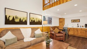 A cozy living room with a brown leather sofa, a wooden coffee table, and a small plant. A wooden cabinet and a microwave are visible in the background. - Twin Pines Lodge #2458 (Big Bear Lake)