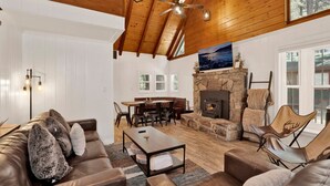 A spacious living room with a stone fireplace, wooden ceiling beams, and a large window. - Twin Pines Lodge #2458 (Big Bear Lake)