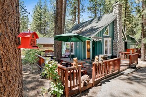 Une cabane rustique avec une cheminée en pierre, une terrasse en bois et une nichoir rouge.