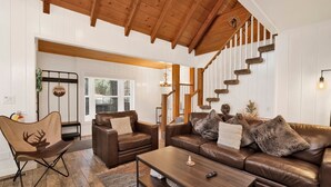 A spacious living room with a high wooden ceiling, a staircase with a rustic design, and leather furniture. - Twin Pines Lodge #2458 (Big Bear Lake)