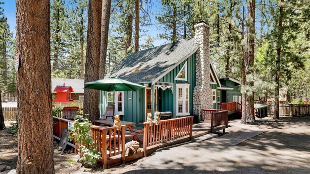 A cabin with a stone chimney, a porch with wooden railings, and a green umbrella. - Twin Pines Lodge #2458 (Big Bear Lake)