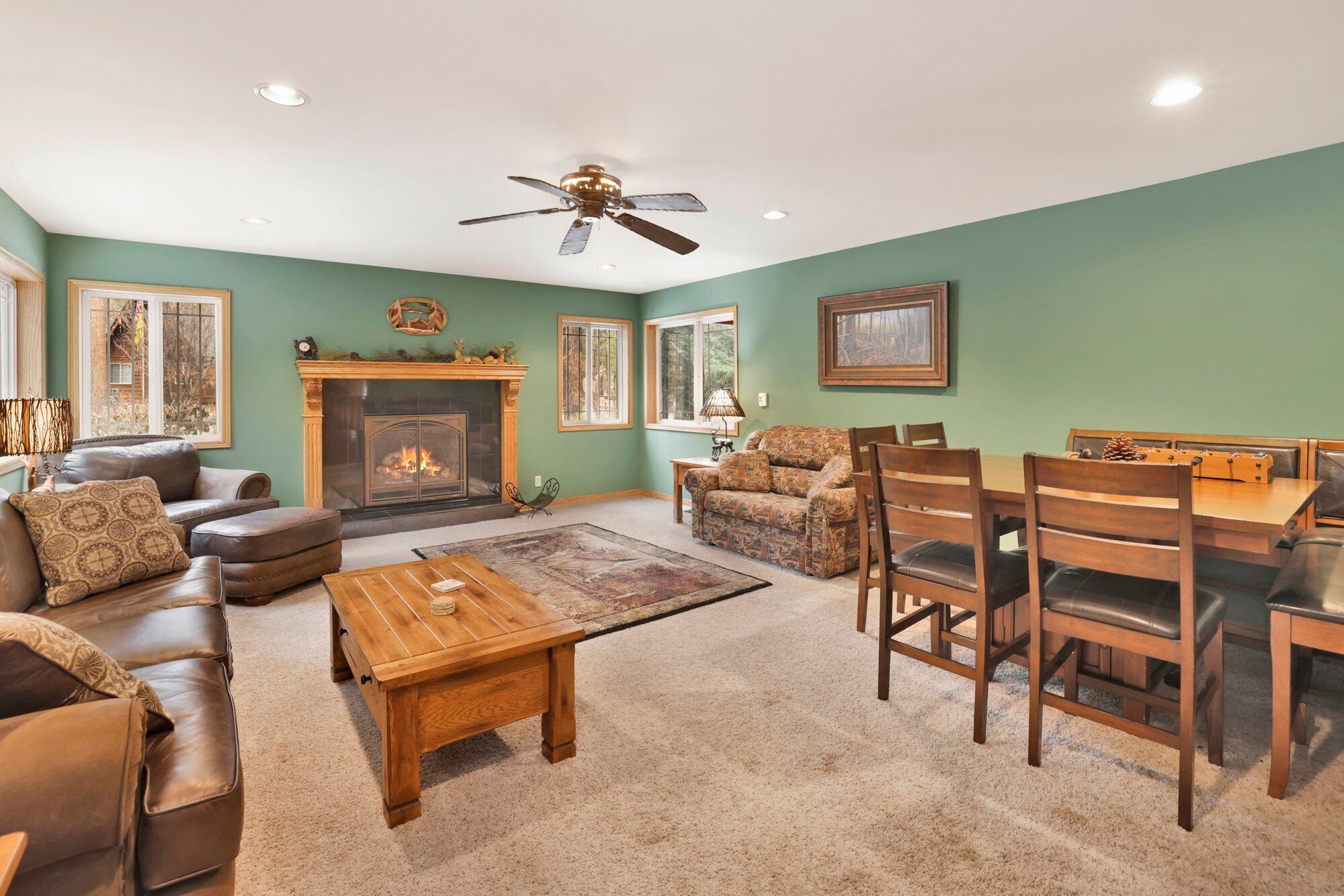 A living room with a fireplace, leather sofas, a dining table with chairs, and a ceiling fan.