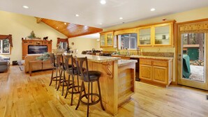 A spacious kitchen with wooden cabinets, a large island with bar stools, and a dining area with a sofa and chairs. - Flitterbick Lodge #2246 (Fawnskin)