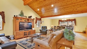 A spacious living room with a wooden ceiling, a large flat-screen TV, a comfortable sofa, and a dining area with a chandelier. - Flitterbick Lodge #2246 (Fawnskin)