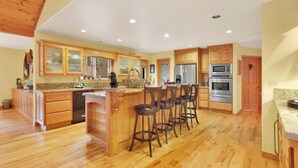 A spacious kitchen with wooden cabinets, a central island with bar stools, a refrigerator, and an oven. - Flitterbick Lodge #2246 (Fawnskin)
