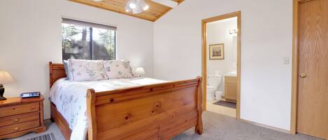 Une chambre à coucher avec un lit en bois, un ventilateur de plafond, une fenêtre et une porte donnant sur une salle de bain.