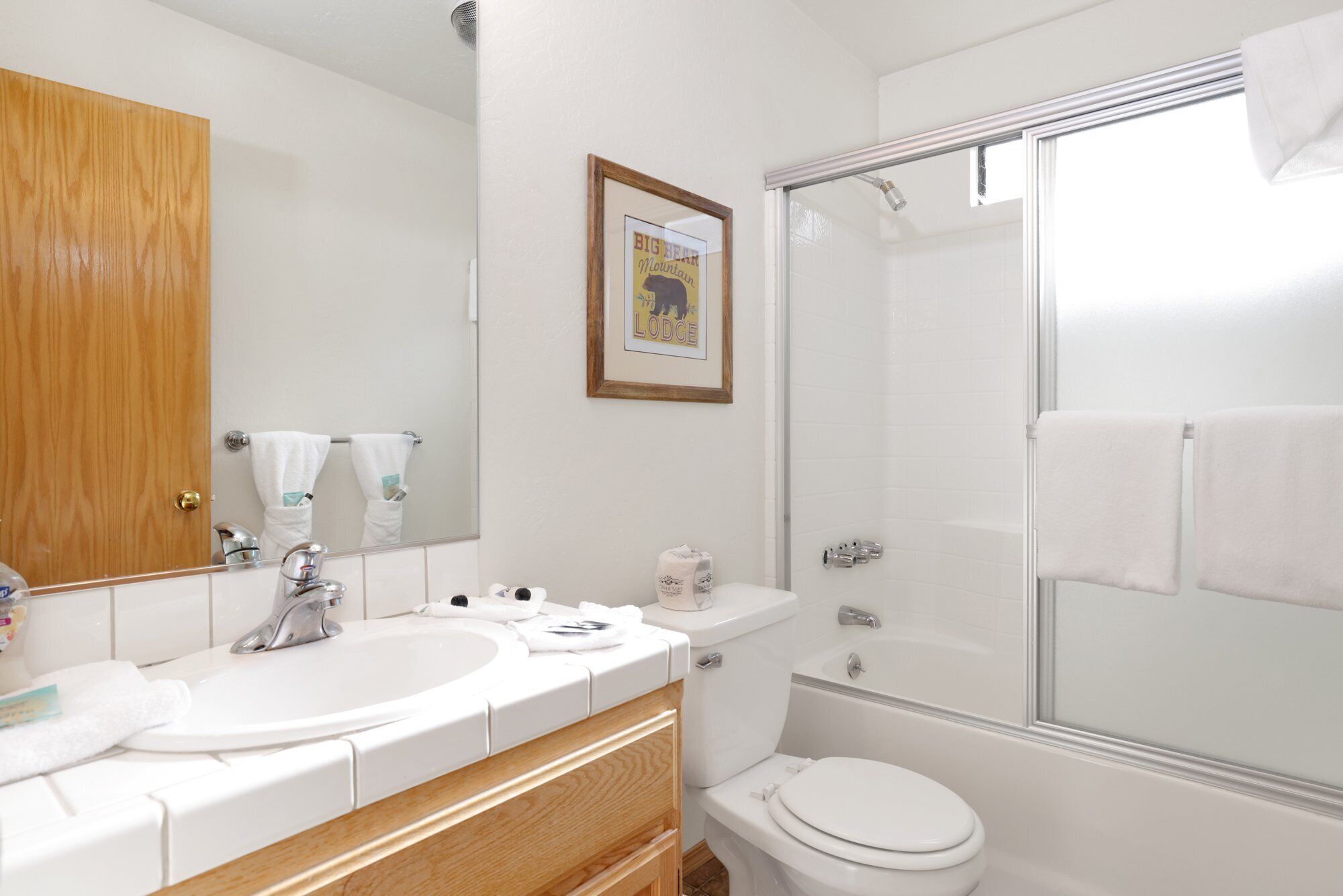 A bathroom with a wooden vanity, a large mirror, a framed picture, a shower, and a toilet.