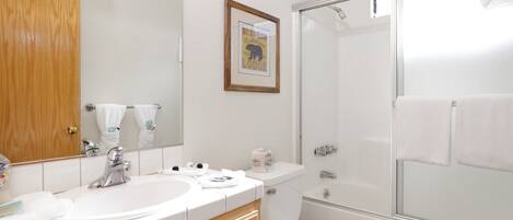 A bathroom with a wooden vanity, a large mirror, a framed picture, a shower, and a toilet.