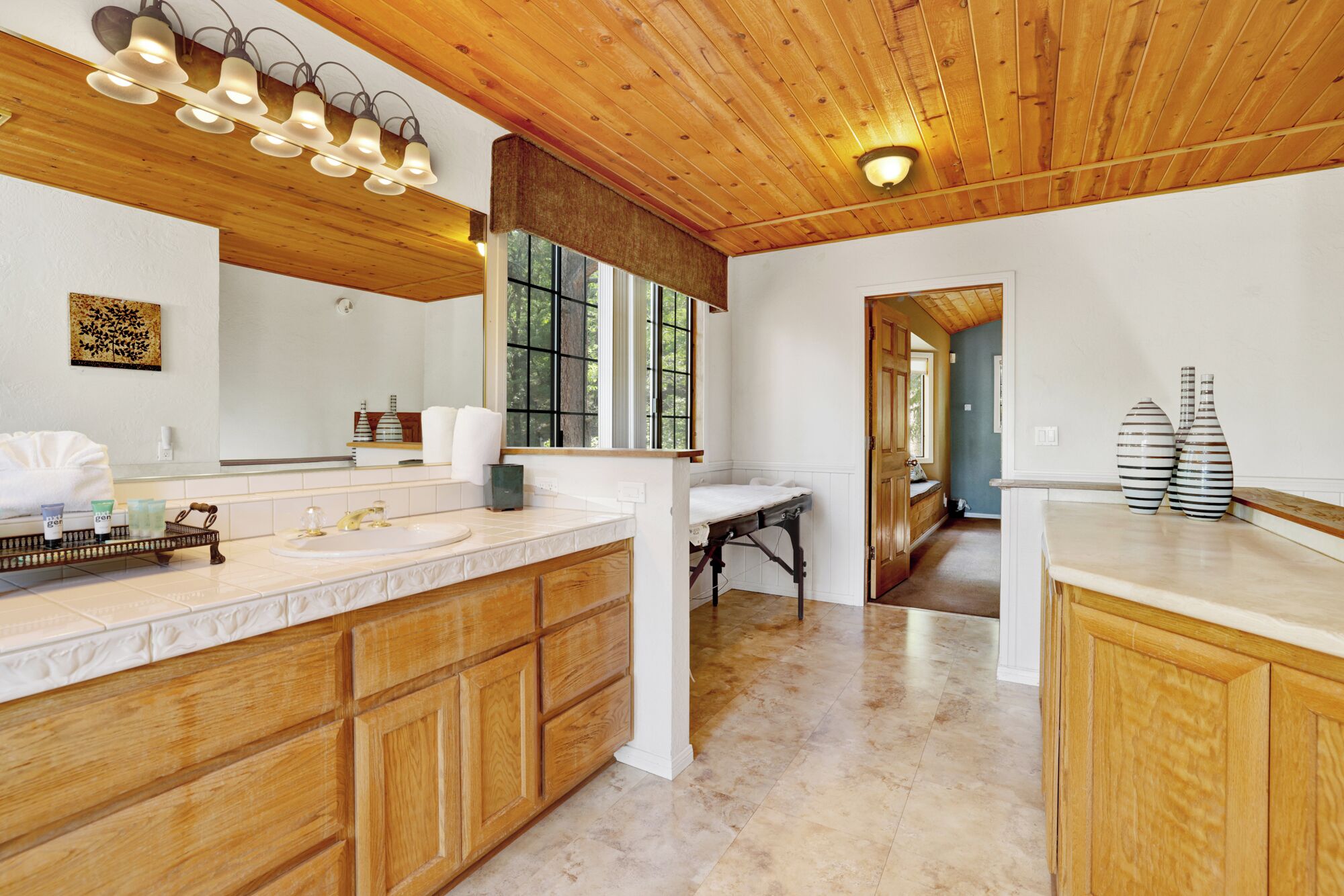 A spacious bathroom with a large wooden vanity, a mirror, and a window providing natural light.