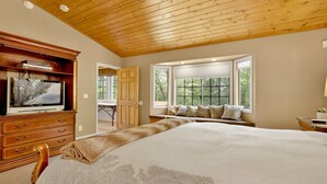 Una camera da letto con un letto grande, soffitto in legno e una finestra vista alberi.