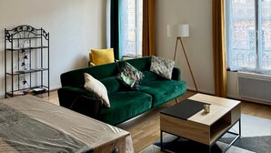 Een woonkamer met een groene bank, een bijzettafeltje, een metalen schapkast en een vloerlamp.