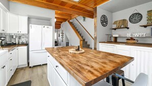 A kitchen with white cabinets, a wooden countertop, a refrigerator, a coffee machine, and a staircase leading to another level.