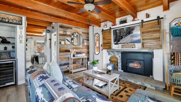 A cozy living room with a fireplace, wooden ceiling beams, and a sofa with patterned cushions.