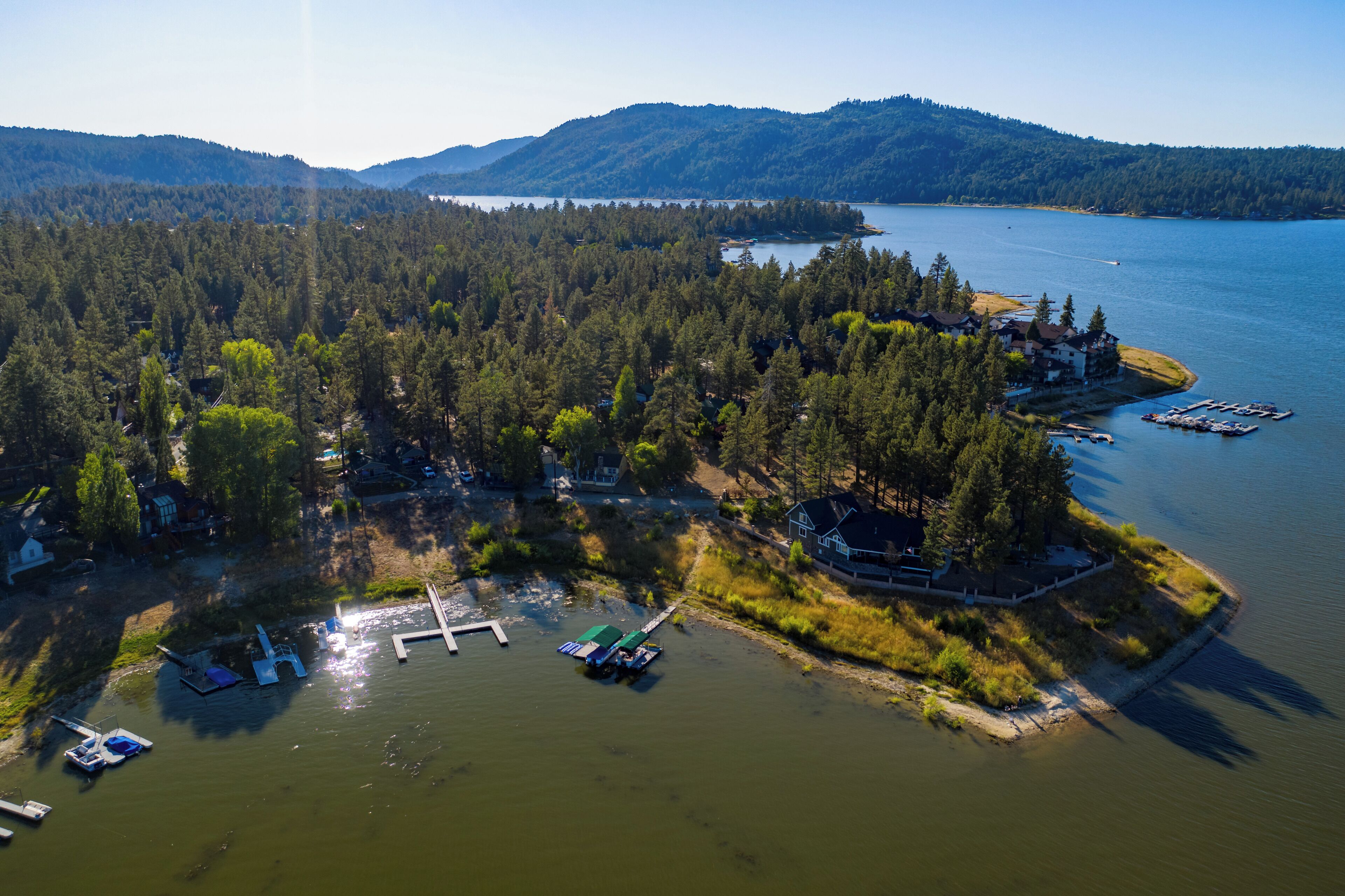 An aerial view of a lakeside property with docked boats, a pier, and a forested area with buildings.