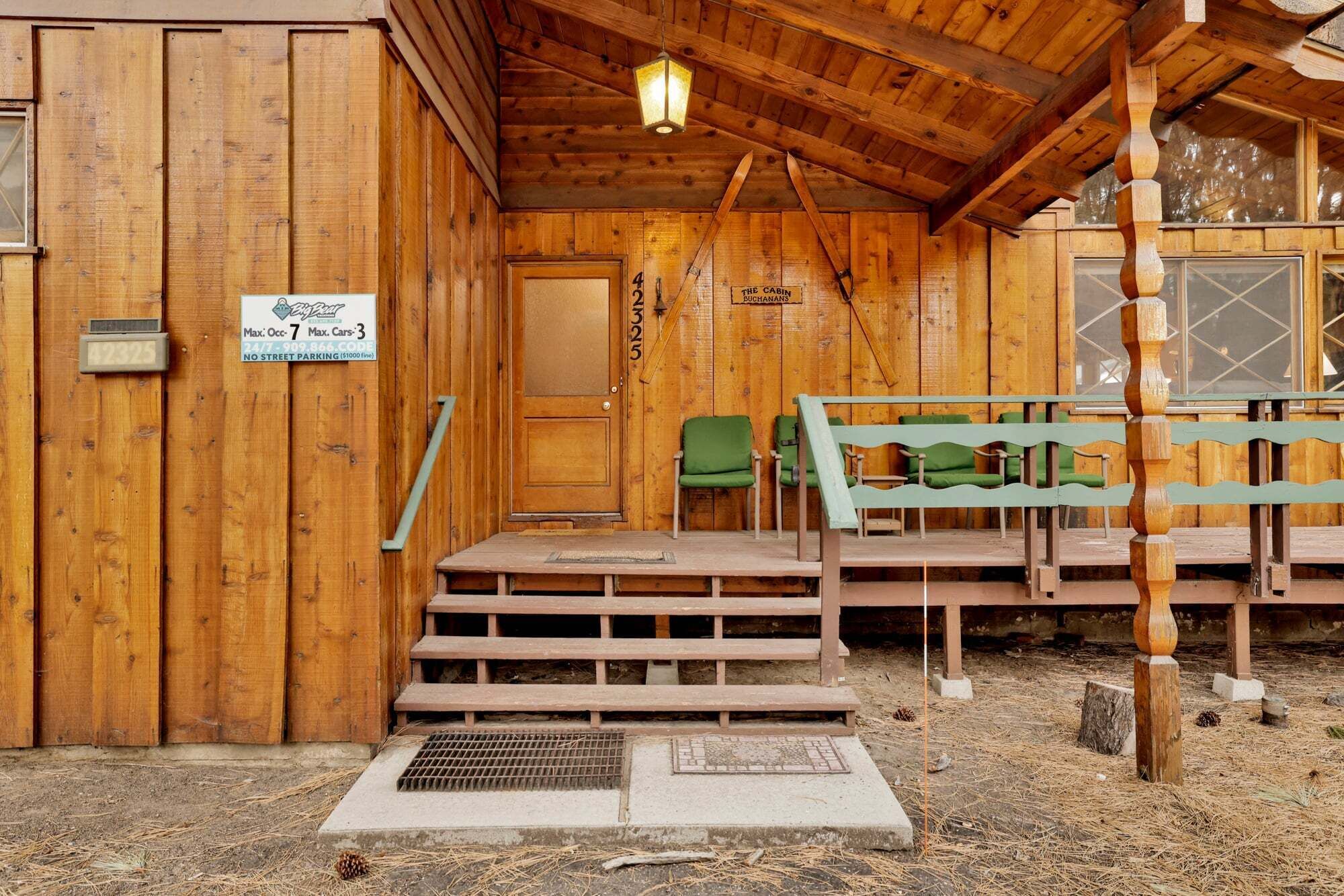 Una cabaña de madera con un letrero que indica 'The Cabin' y 'The Cabin' en la puerta. Hay escalones que conducen a un porche con sillas verdes.
