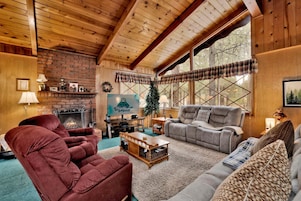 A cozy cabin interior with a fireplace, wooden walls, and large windows.