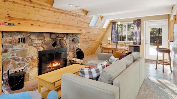 Una sala de estar acogedora con chimenea de piedra, techo de madera y un comedor con mesa y sillas.
