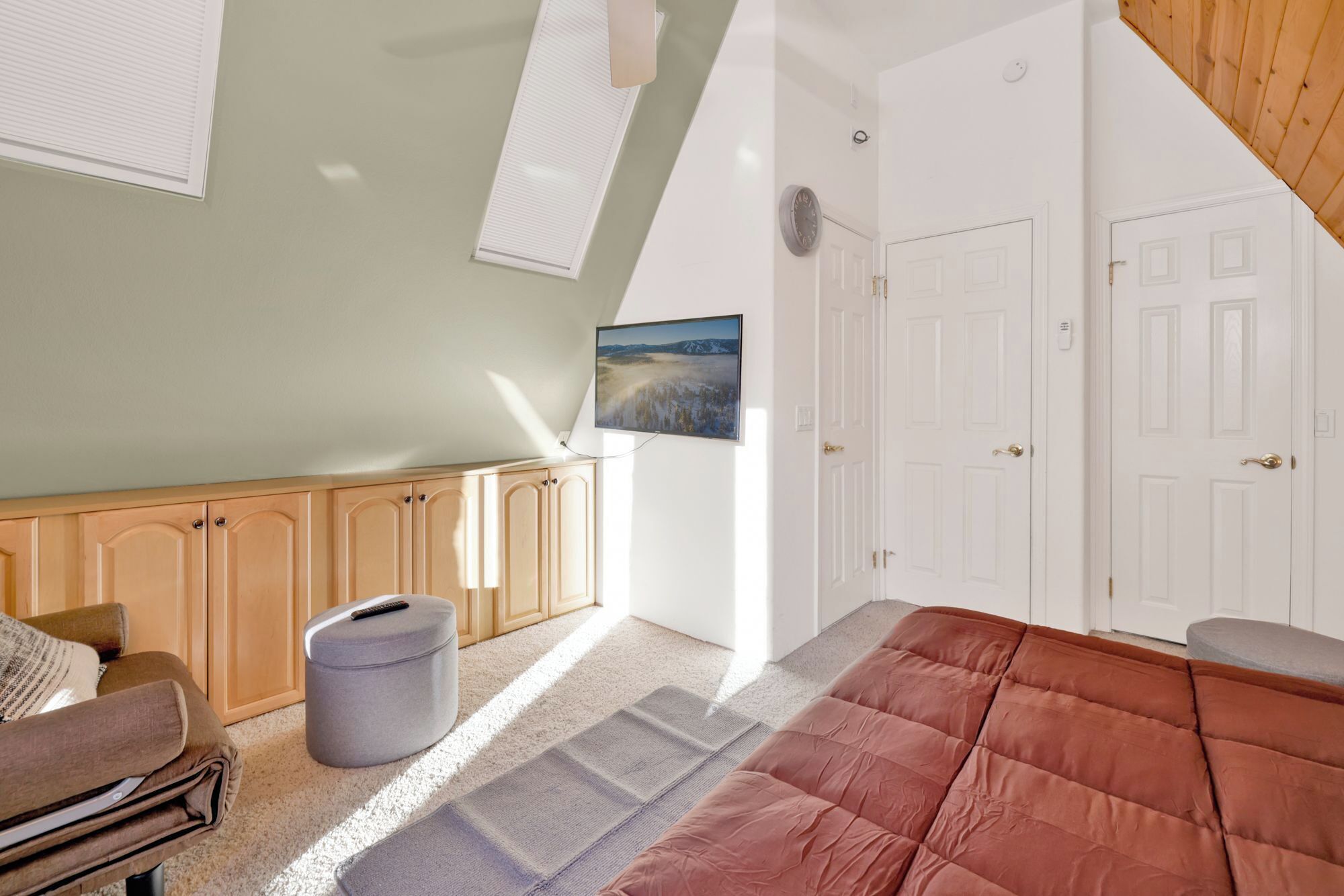 A bedroom with a sloped ceiling, a bed, a sofa, a waste bin, and a painting on the wall.