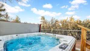 A hot tub with a control panel, surrounded by a wooden deck and a chain-link fence, with trees in the background. - A Hidden Asset #2379 (Big Bear Lake)