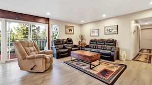 A spacious living room with a large window, a fireplace, and a cozy seating area with leather sofas and a recliner. - A Hidden Asset #2379 (Big Bear Lake)