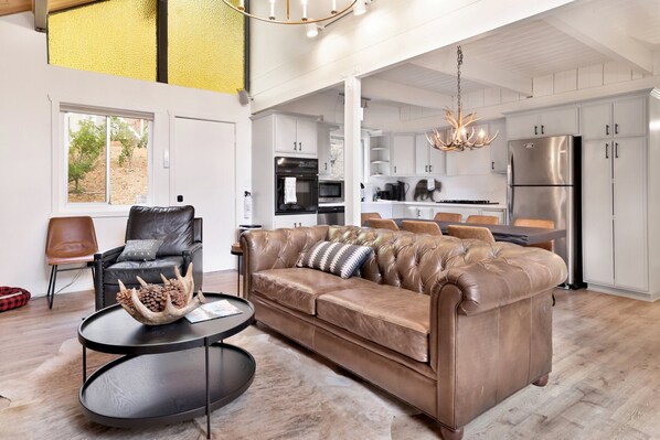 A modern living room with a brown leather sofa, a round black coffee table, and a chandelier.