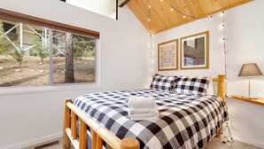 A bedroom with a checkered bedspread, a wooden headboard, a bedside table with a lamp, and two framed pictures on the wall.