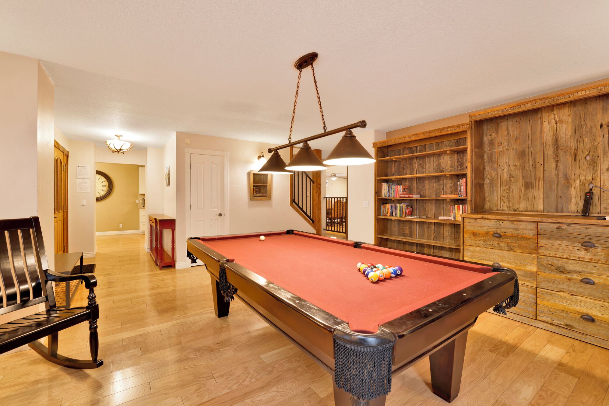 A pool table with a red felt surface, wooden bookshelves, and a wooden bench.
