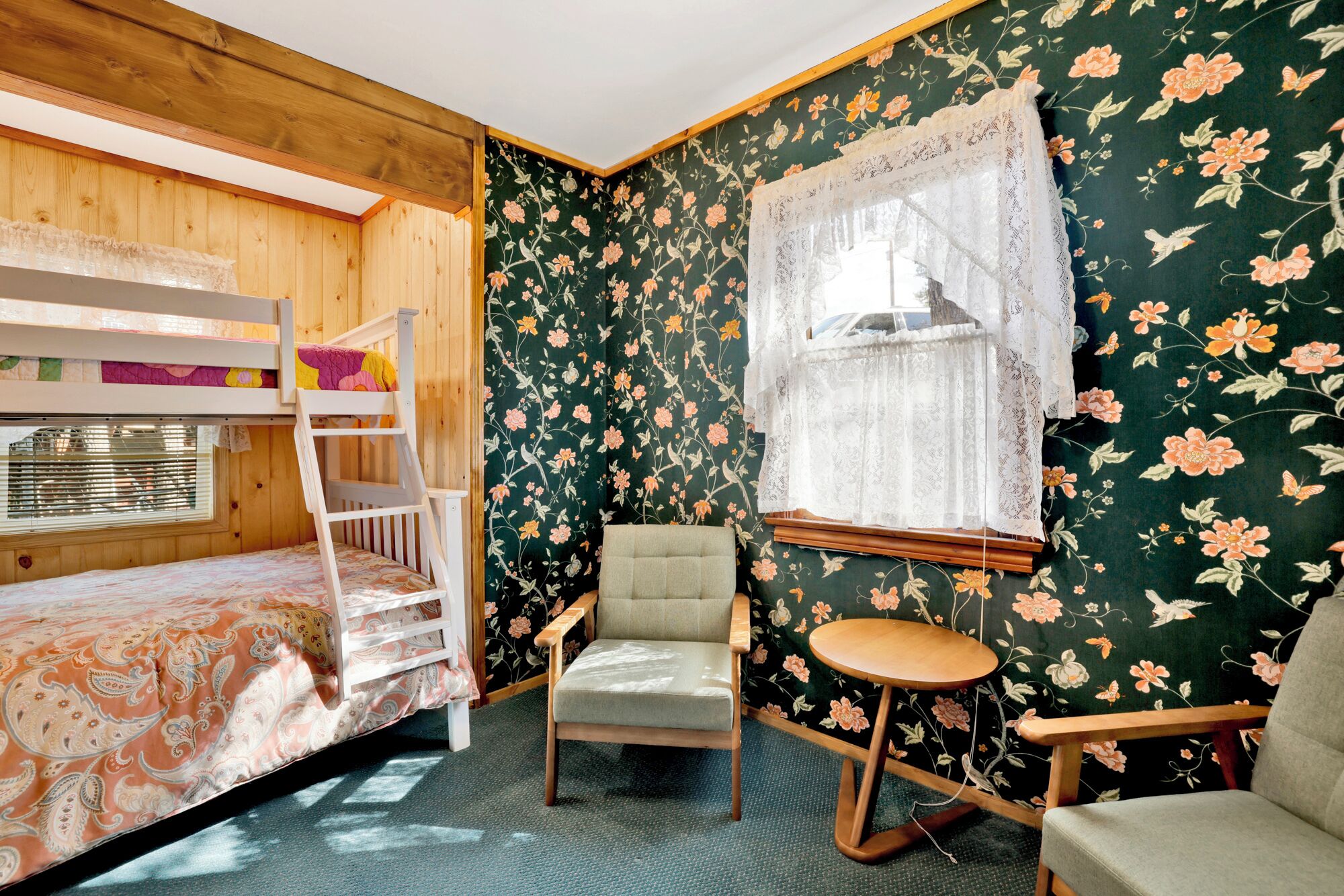 Une chambre avec un lit superposé, une chaise, une petite table ronde et une fenêtre ornée de rideaux en dentelle.