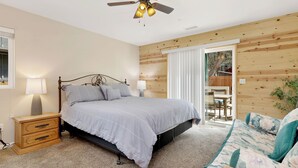 A bedroom with a bed, bedside tables, a ceiling fan, and a view of an outdoor patio.