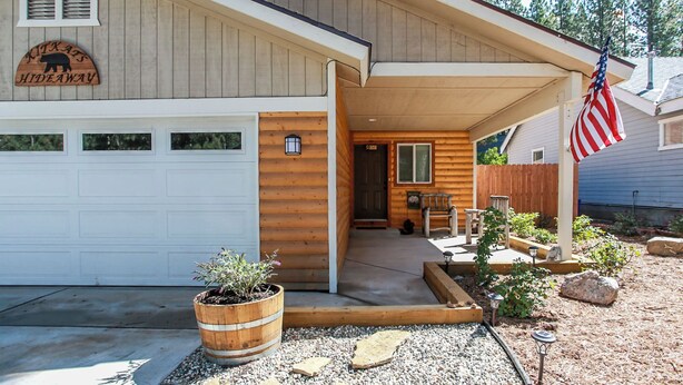 A log cabin with a covered porch, a wooden front door, and an American flag.
