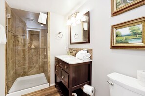 A bathroom with a glass-enclosed shower, a vanity with a mirror, and a toilet.