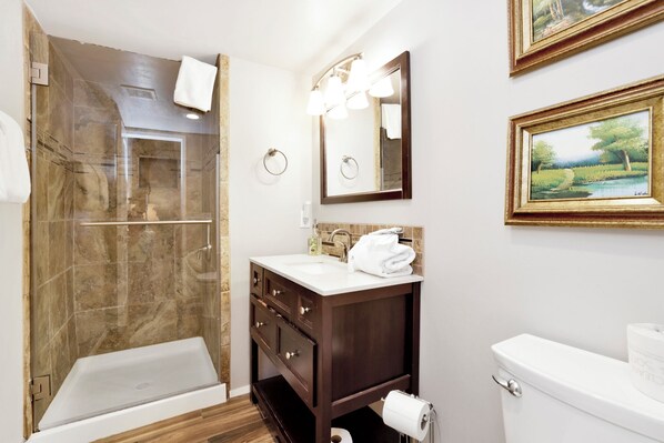 A bathroom with a glass-enclosed shower, a vanity with a mirror, and a toilet. - Smith Summit Chalet #2461 (Big Bear Lake)
