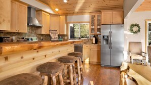 A cabin-style kitchen with wooden cabinets, a stainless steel refrigerator, and a bar area with stools. - Silver TIP Chalet #2141 (Big Bear Lake)