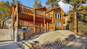 A two-story log cabin with a wooden deck and a stone retaining wall. - Silver TIP Chalet #2141 (Big Bear Lake)